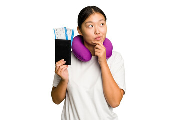 Young asian woman with inflatable travel pillow on her neck holding passport isolated looking sideways with doubtful and skeptical expression.