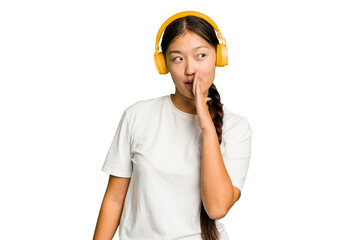 Young asian woman listening to music with headphones isolated is saying a secret hot braking news and looking aside