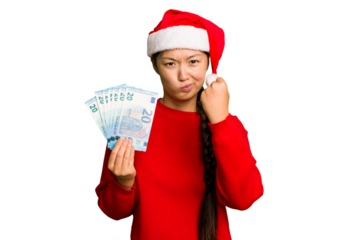 Young asian woman celebrating Christmas holding banknotes isolated showing fist to camera, aggressive facial expression.