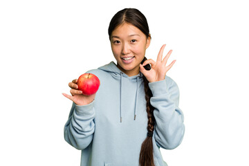 Young asian woman holding a red apple isolated cheerful and confident showing ok gesture.