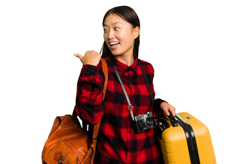 Traveler asian woman holding a suitcase isolated points with thumb finger away, laughing and...
