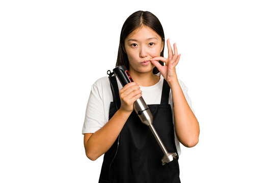 Young asian cook woman holding a blender isolated with fingers on lips keeping a secret.