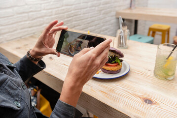 hands holding up a smartphone taking a picture of a vegan burger