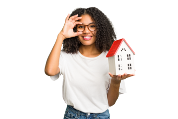 Young african american woman moving to a new home while picking up a box full of things isolated excited keeping ok gesture on eye.