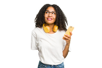 Young african american woman listening to music with yellow headphones isolated dreaming of achieving goals and purposes