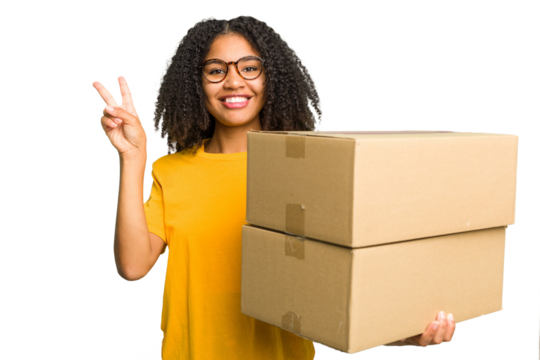 Young african american woman moving to other house while picking up a box full of things isolated joyful and carefree showing a peace symbol with fingers.