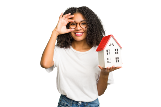 Young african american woman moving to a new home while picking up a box full of things isolated excited keeping ok gesture on eye.