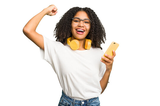Young african american woman listening to music with yellow headphones isolated raising fist after a victory, winner concept.