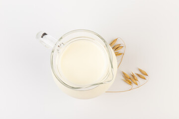 Oat milk in a jug and oat spike on light background. Vegan non dairy alternative milk.
