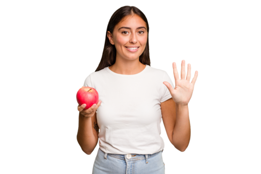 Young caucasian woman holding a red apple isolated smiling cheerful showing number five with fingers.