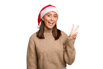 Young caucasian woman celebrating christmas wearing a santa hat isolated joyful and carefree showing a peace symbol with fingers.