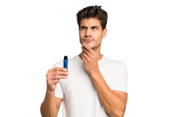Young caucasian man holding an electronic cigarette isolated looking sideways with doubtful and skeptical expression.