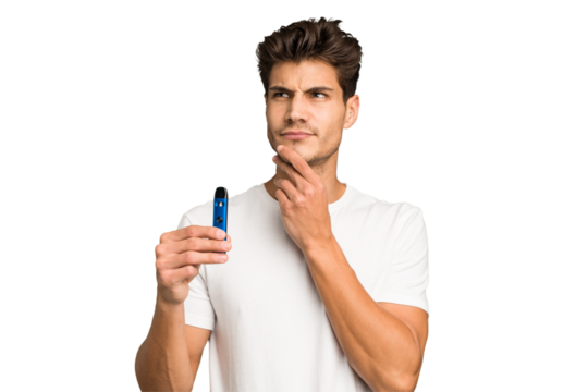 Young caucasian man holding an electronic cigarette isolated looking sideways with doubtful and skeptical expression.