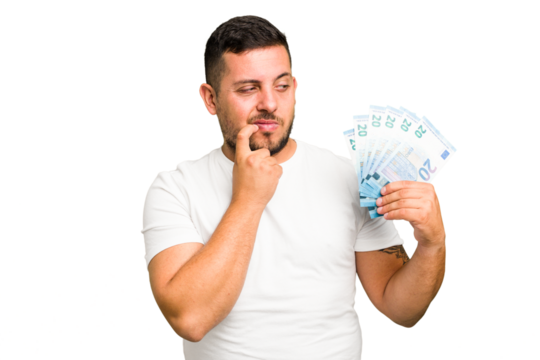 Young caucasian man holding a banknotes isolated relaxed thinking about something looking at a copy space. - Powered by Adobe