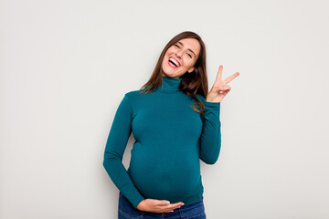 Pregnant caucasian woman isolated on white background joyful and carefree showing a peace symbol...