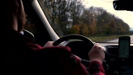A man is driving a car along a road during the autumn season