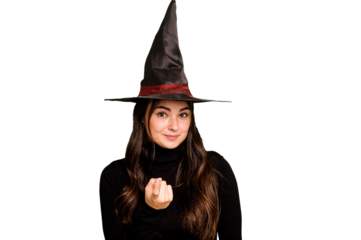 Young caucasian woman dressed as a witch isolated on green chroma background pointing with finger at you as if inviting come closer.