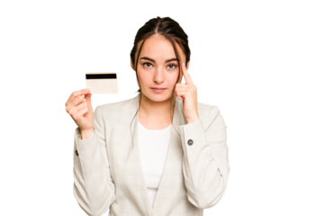 Young caucasian woman holding a credit card isolated on green chroma background pointing temple with finger, thinking, focused on a task.