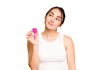 Young caucasian woman holding menstrual cup isolated on green chroma background dreaming of...