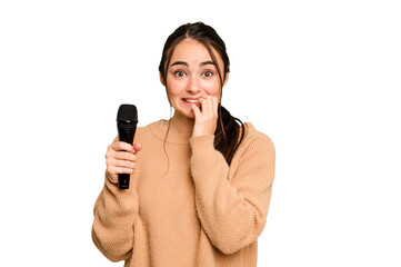 Young caucasian singer woman isolated on green chroma background biting fingernails, nervous and...