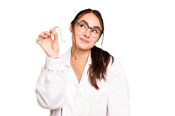 Young otorhinolaryngologist holding hearing aid isolated on green chroma background dreaming of...