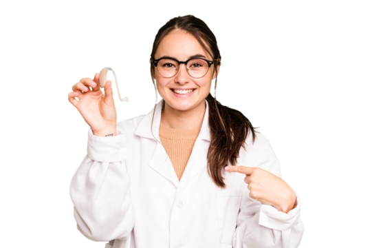 Young otorhinolaryngologist holding hearing aid isolated on green chroma background person pointing by hand to a shirt copy space, proud and confident