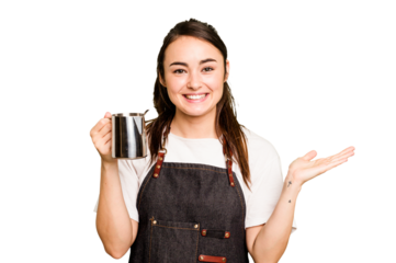 Young barista woman isolated on green chroma background showing a copy space on a palm and holding another hand on waist.