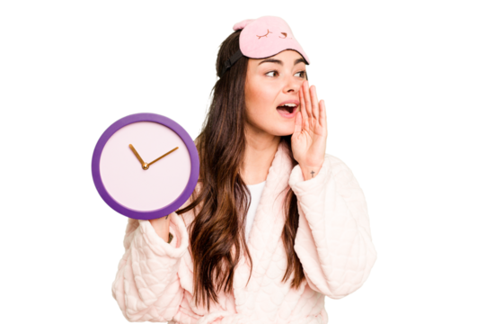Young caucasian woman holding a clock wearing a pajama isolated on green chroma background shouting and holding palm near opened mouth.