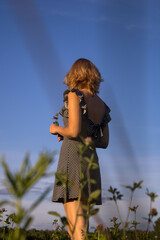 a woman in a black sundress with her hair down stands with her back in a field against a blue sky with grass in the foreground