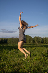 a woman jumps in flight hands in different directions in a summer field in a black sundress