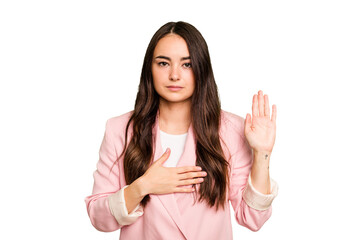 Young caucasian woman isolated on green chroma background taking an oath, putting hand on chest.