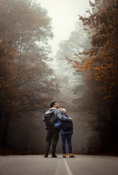 Rear view of couple spending time together walking on forest road on a foggy morning.
