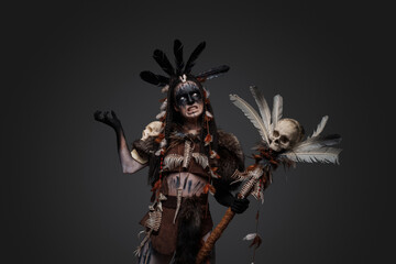Shot of angry dark sorcerer dressed in aboriginal attire against grey background.