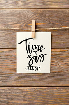 Time to say goodbay. A handwritten inscription on a piece of paper that hangs on a rope. Brown wooden background.