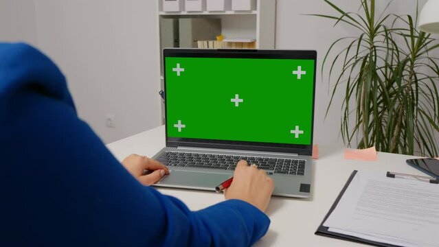 Woman watching webinar on laptop computer with mock up green screen chroma key display. Office worker spending break time by using browsing on internet.