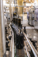 Dark glass bottles being filled with wine by industrial bottling machine at modern wine factory