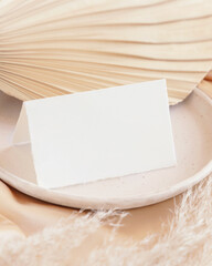 Folded card near dried palm leaf and beige silky fabric close up, greeting or wedding mockup