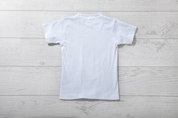 Back view of boys t-shirt on white wooden table background top view. Mockup for design close up