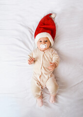 baby in a New Year's hat and with a pacifier lies on the bed