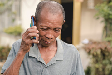 A bald filipino male in his early 60s ardently listens to his cellphone. Having a long distance chat. Scene outside his home.