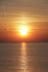 Vertical photo of the sun setting in the ocean during golden hour