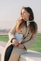 Close-up of thoughtful mid adult woman with curly hair looking away at park. Dreamy woman in beige coat autumnal park.