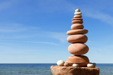 Fototapeta na wymiar High Rock zen pyramid of pink stones on a background of blue sky and sea.