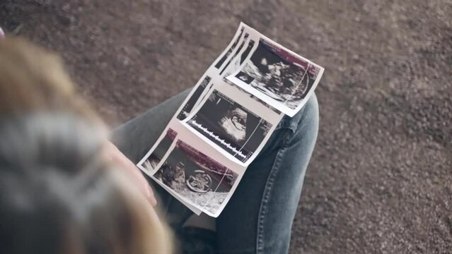 Happy woman enjoying her ultrasound scan pictures of her baby boy or girl, medical examination for baby gender reveal, young mom stroking her beautiful round belly with tenderness and affection