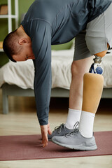 Vertical portrait of man with prosthetic leg working out at home and doing stretching exercises