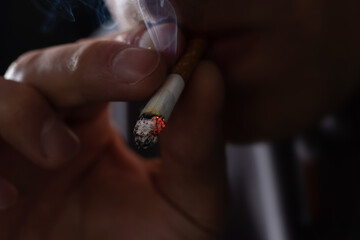 Man smoking a cigarette on black background. close up