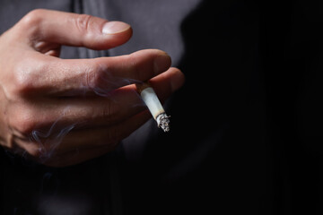 Hand with burning cigarette and smoke on black background