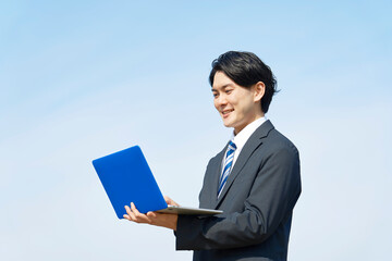 外でノートパソコンを使うビジネスマン　青空背景