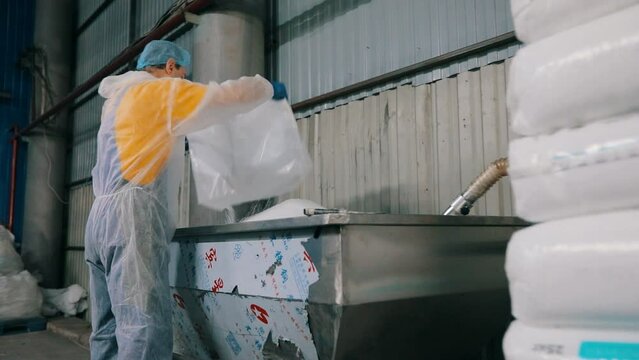 A worker pours polypropylene grains into a machine. A worker pours polypropylene from a bag. Production of nonwoven materials