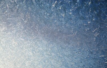 Blaue Glasscheibe mit Wellenförmigem Eismuster bei Frost und Sonne am Morgen im Winter